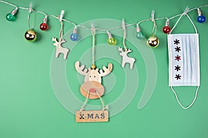 Decorative reindeer in a garland of colored lights with a surgical mask on a green background