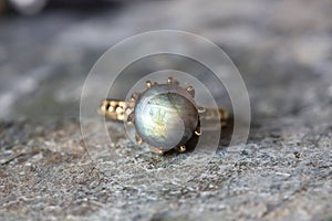 decorative ring with natural mineral labradorite gemstone on grey neutral rocky background
