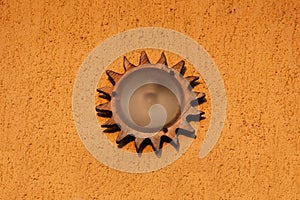 Decorative round outside light fixture with wooden frame resembling sun rays mounted on house wall with yellow facade