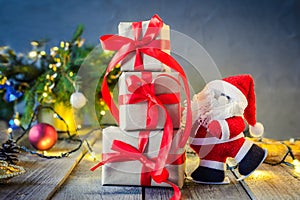 Decorative Santa Claus carrying presents on the festive dark background with Christmas tree, lights and decor on the old wooden bo