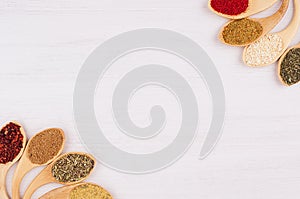 Decorative semicircle of different spices in bamboo spoons on white wood background, top view, closeup.