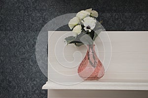 Decorative shelf on gray wall with flower in a vase on it