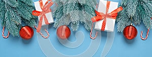 Decorative spruce branches with red balls, gift boxes and candy cane on a blue paper background. Beautiful Christmas