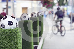 Decorative stand with football ball in the net on the green grass. Ornaments of city streets. Blurred people, man on a