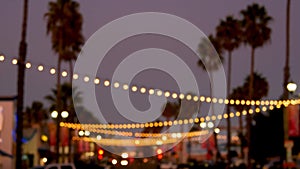 Decorative staring garland lights, palm trees silhouettes, evening sky. Blurred Background. Street decorated with lamps in