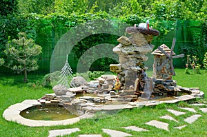Decorative stone fountain with water mill and garden figurines. Landscape design.