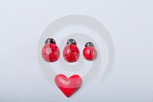Decorative tiny red ladybugs with red heart on fair background. Love, full family with one child, motherhood, parents