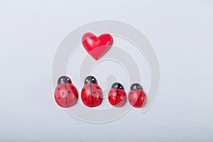 Decorative tiny red ladybugs with red heart on fair background. Love, full family with two children, motherhood, parents