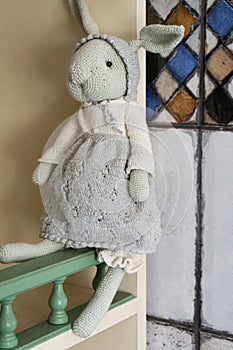 A decorative vintage handmade knitted toy rabbit in a hat, skirt and light blouse sits on the shelf of a children's locker.