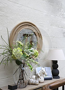 Decorative wall decoration: a mirror, a console with a lamp, flowers and trinkets.