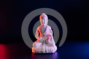 Decorative white Buddha statuette on the dark background in red and blue neon light. Duality concept, Yin Yang. internal