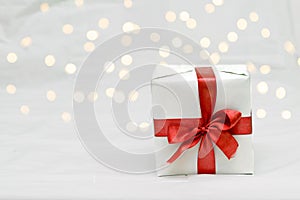 Decorative white gift box with a large red bow against a background bokeh of lights