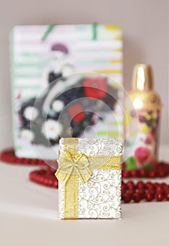 Decorative white gift box with a yellow bow on the background of a parfume and red beads