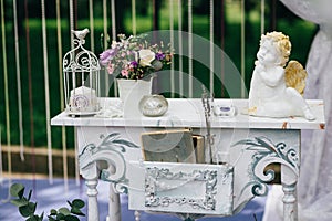 Decorative white vintage table at the wedding ceremony, candle-decorated books with flowers and ceramic angles and