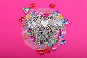 Decorative wicker heart surrounded with coloured hearts. Heart shaped gems on crimson background and wicker heart in center, top