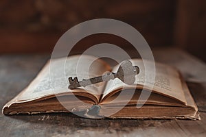 A decorative wooden key rests on an open old vintage book on a dark background