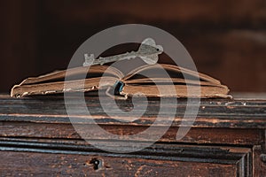 A decorative wooden key rests on an open old vintage book on a dark background