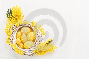 Decorative yellow Easter eggs and mimosa wreath on a white background. Flat lay, copy space for text