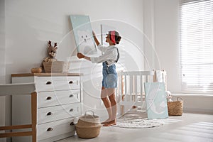 Decorator hanging picture on white wall in baby room. Interior design