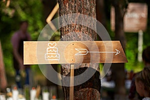 Decoratoration wooden wedding cake arrow sign in the pine forest. Cake banner on event venue in the woods outdoors.