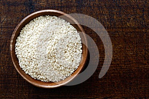 Decorticated sesame seeds in dark wooden bowl isolated on dark b