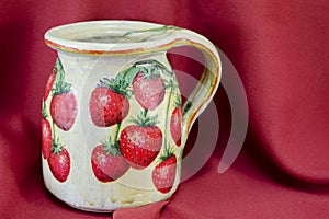 Decoupage decorated strawberry pattern pitcher on red fabric bac