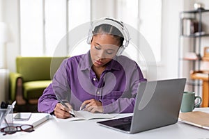 Dedicated black female student taking notes from an online class