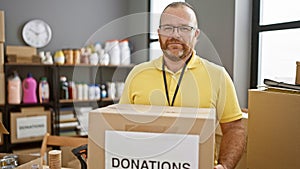 Dedicated caucasian male volunteer handsomely stands holding donations package at community charity center in warehouse-like room