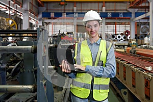 A dedicated female engineer dressed in safety gear, holding laptop computer amidst a sprawling factory