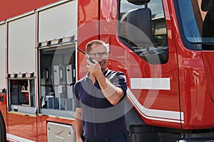 A dedicated firefighter, captured in a moment of communication, stands before a modern firetruck, showcasing the