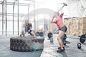 Dedicated man and woman hitting tire with sledgehammer in crossfit gym