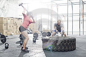 Dedicated man and woman hitting tire with sledgehammer in crossfit gym photo