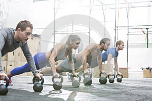 Dedicated people doing pushups with kettlebells at crossfit gym photo