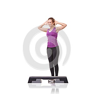 Dedicated to better fitness. A smiling young woman doing aerobics on an aerobic step against a white background.