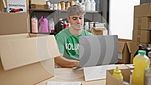 Dedicated young hispanic man concentrates as he sits at the table, volunteering, working online on his laptop at a bustling