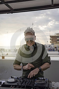 Deejay mixing outdoor with back sun light - Portrait of disc jockey playing disco or deep music for people on beach party at