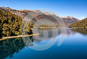 Deep blue lake reflecting sky and vegetation.Mountains in the back