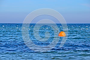 Deep blue ocean withan orange buoy and some white seagulls swimming on it and a wide horizon