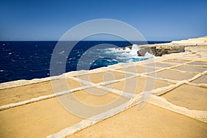 Deep blue sea, horizon and sky with yellow-brown sand stone shore foreground. Salt ponds in Gozo island, Malta.