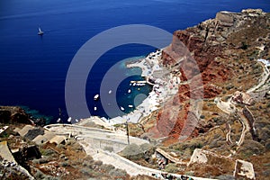 Deep blue sea and steep red mountain with a serpantine road. Santorini Island, Greece