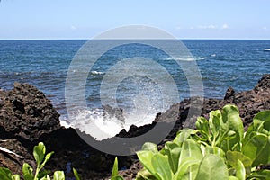 Deep blue water of the Pacific Ocean crashing into the rocky, volcanic shoreline at Onomea Bay