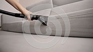 Deep cleaning of a sofa with a machine. Close-up of a housekeeper holding a modern washing vacuum cleaner and cleaning a