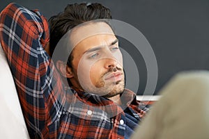 Deep contemplation. A gorgeous young man lying on a sofa with his arm behind his head.