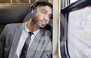 In deep contemplation during his commute. a young businessman wearing headphones while staring out the window on a train