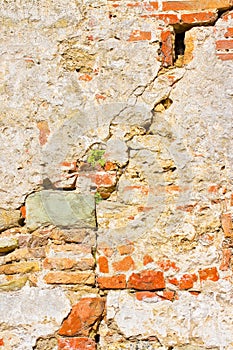 Deep crack in old brick and stone wall with damaged plaster