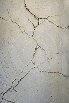 Deep cracks on the plastered and painted dirty concrete wall