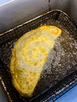 Deep-fried chebureks in nature. The process of cooking meat pies in a cast-iron frying pan in hot oil. Camping food