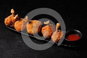 Deep-fried chicken legs and tomato sauce on black plate on black background