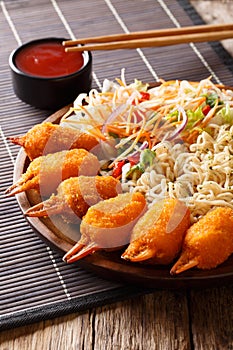 Deep fried crab claws in a breading, udon noodles and fresh vegetable salad close-up on a plate. vertical