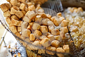 Deep fried cubic cut tofu on metal net over hot oil pan.